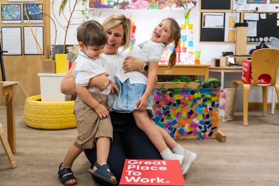 A woman and two children in a classroom with a great place to work sign.