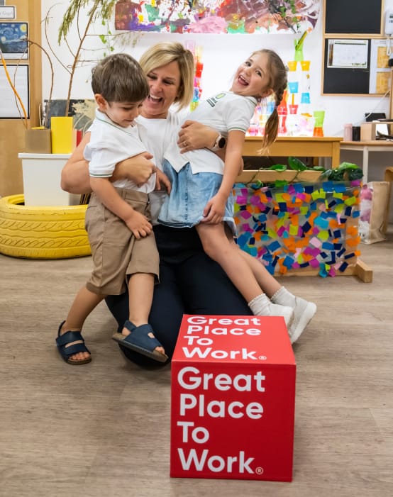A woman and two children in a classroom with a great place to work sign.