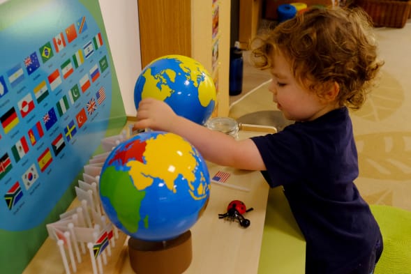 A young child playing with a globe in a playroom.