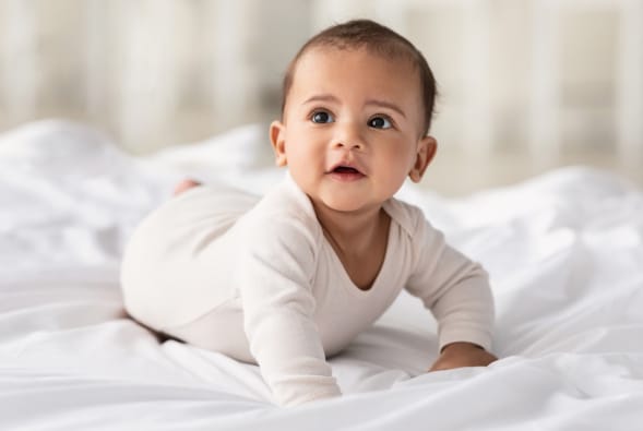 A baby is laying on a white bed.