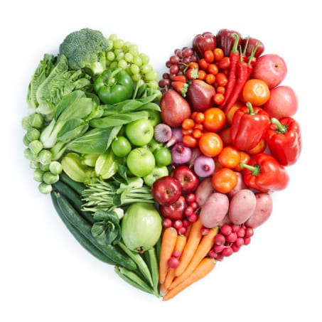 A heart shaped arrangement of fruits and vegetables on a white background.
