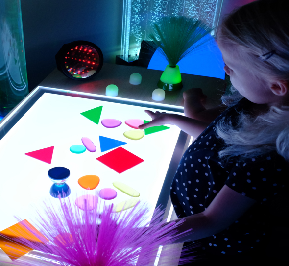 A little girl playing with a colorful light table.